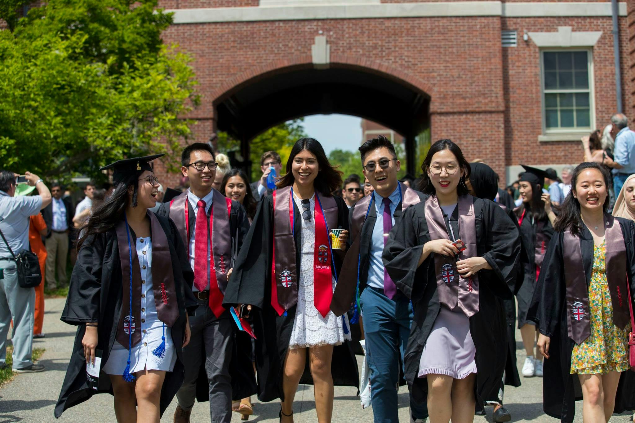 A group of students walking at Brown University wearing graduation gowns.