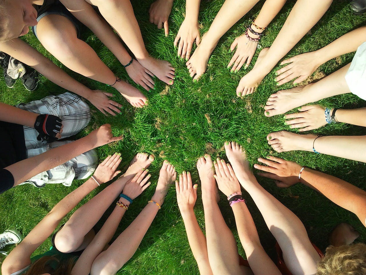 Several people with their feet and hands out forming a circle in the grass.