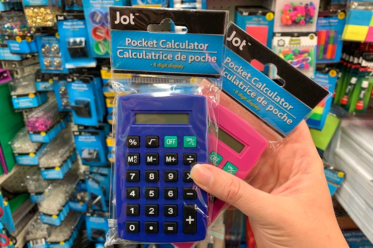 A person's hand holding two Pocket Calculators in front of a shelf inside Dollar Tree.