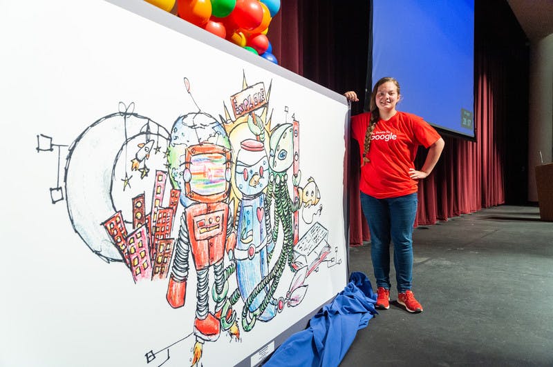 A student standing next to her winning Doodle for Google drawing on a stage.