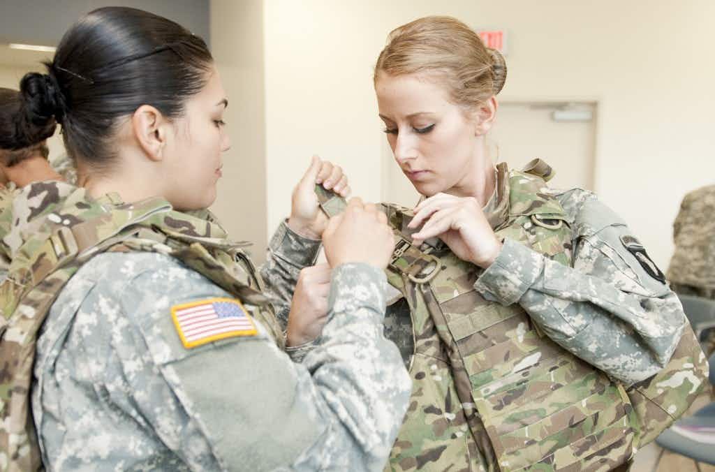 Two woman in military uniform putting on combat vests.