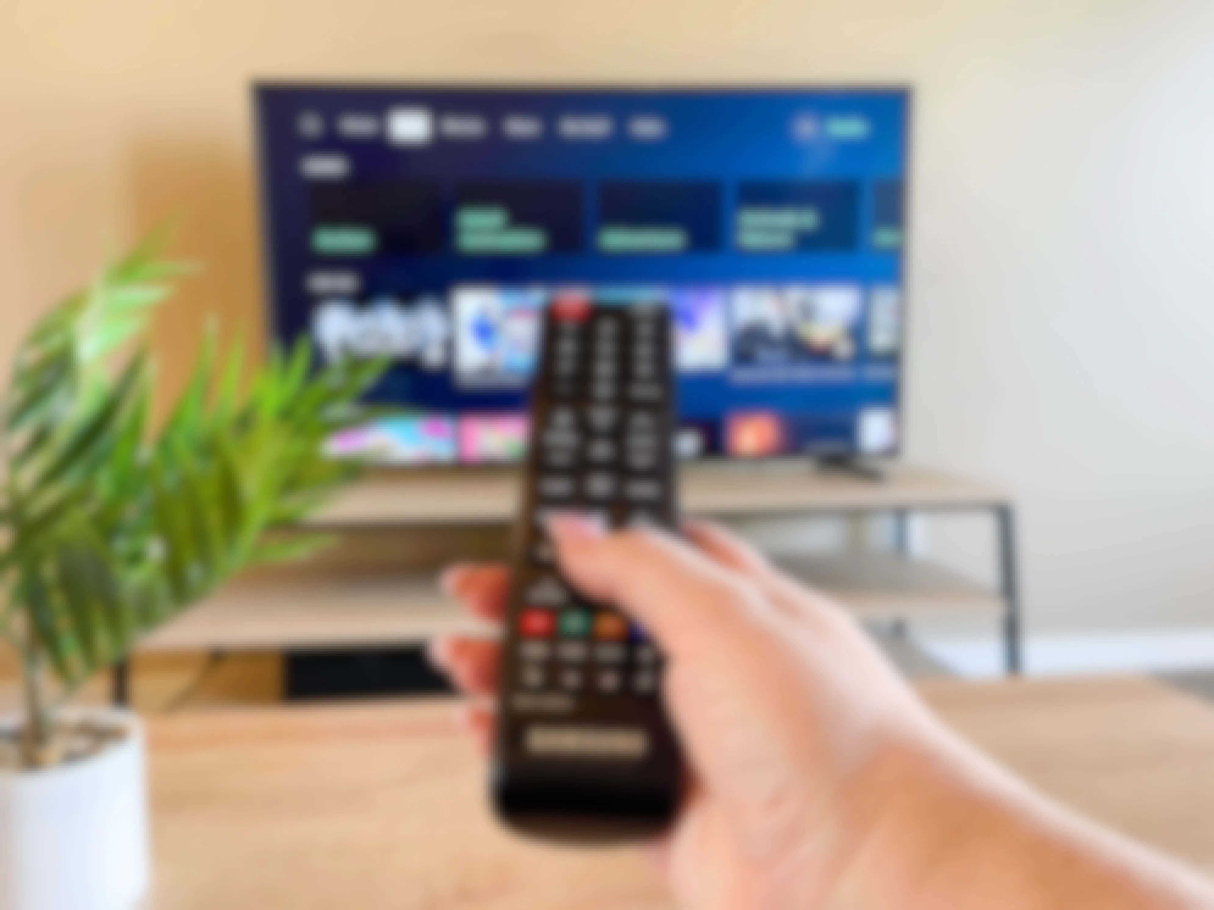 woman's hand pointing remote toward TV with hulu app