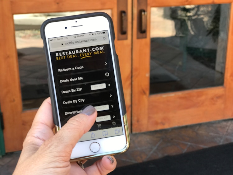 A person's hand holding up their iPhone which has Restaurant.com opened in the mobile internet browser app.