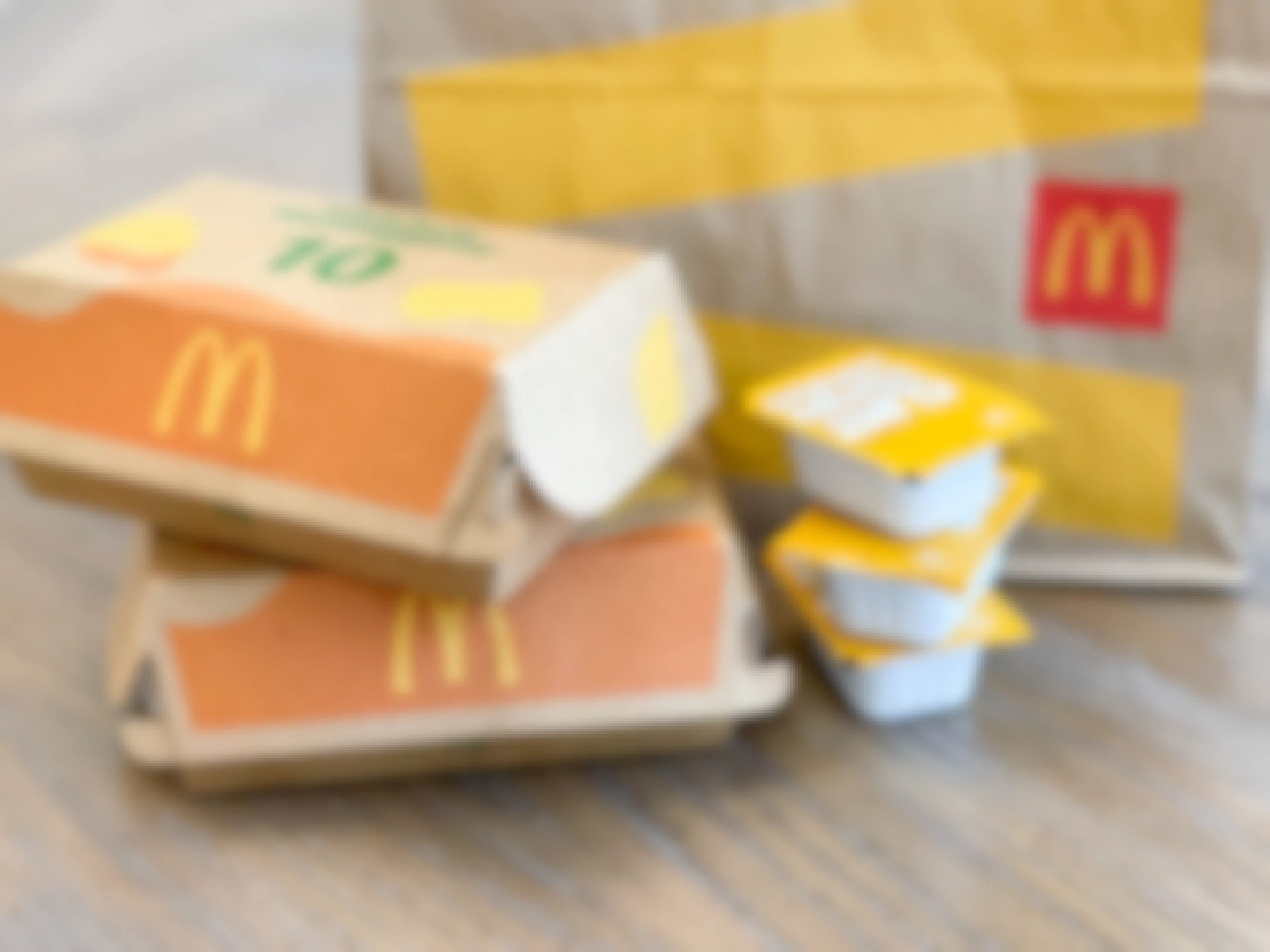 Two 10 piece chicken McNugget boxes stacked on a table next to a stack of honey mustard sauces and a McDonald's bag.