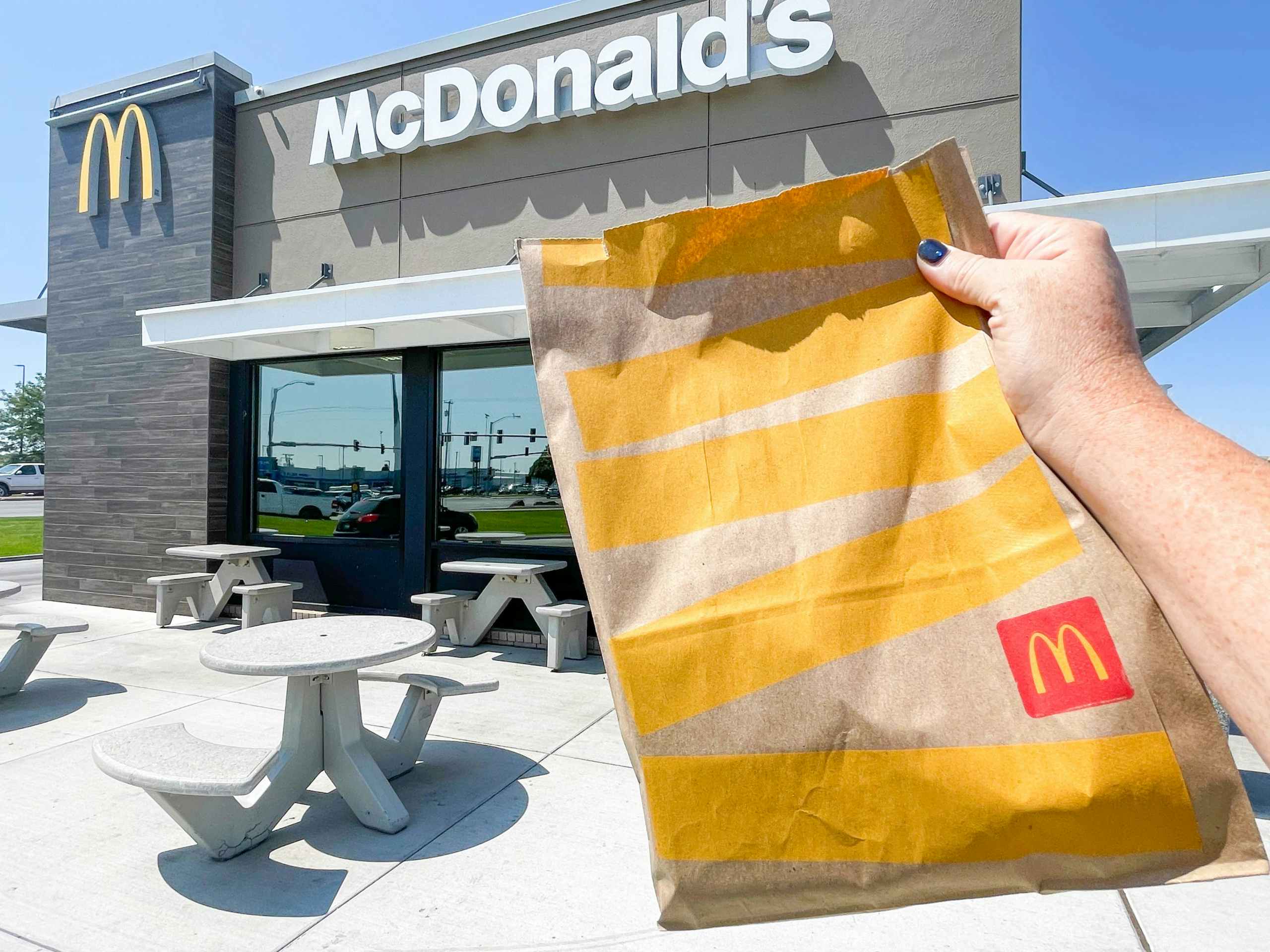 A person holding a bag of McDonalds take out in front of a restaurant.