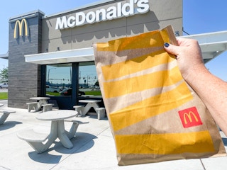 A person holding a bag of McDonalds take out in front of a restaurant.