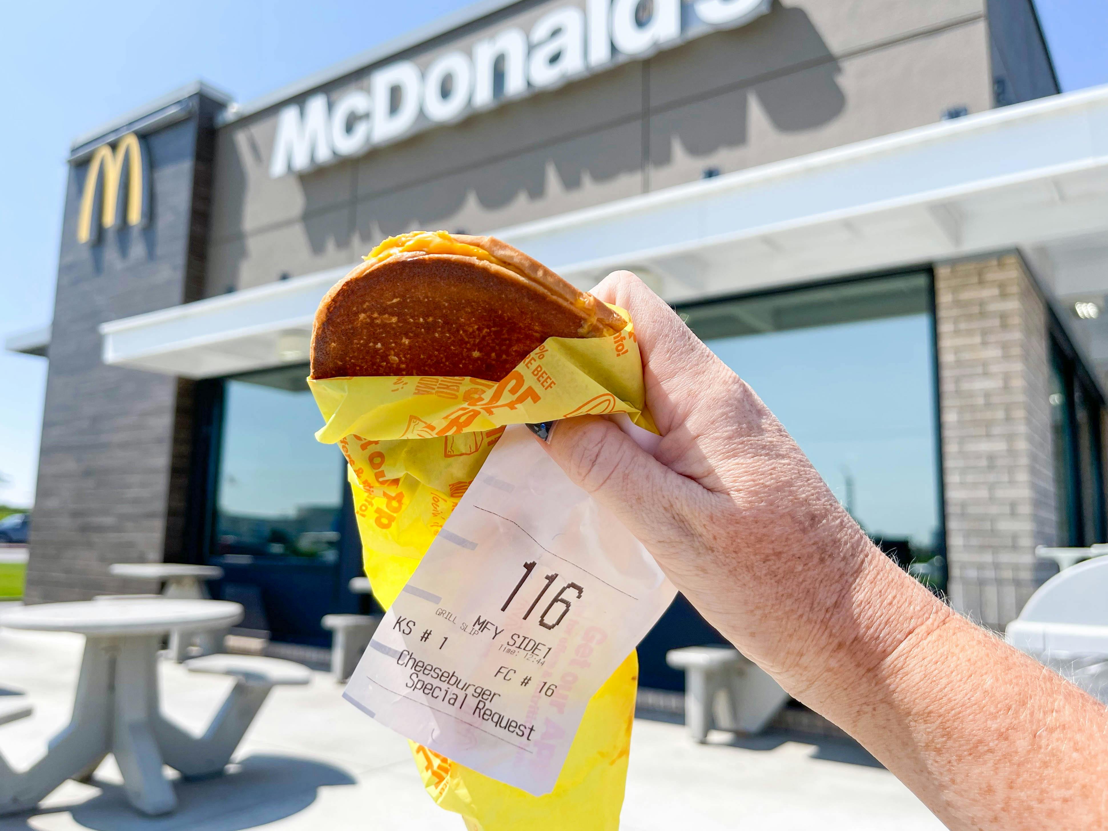 A person's hand holding a specially requested McDonald's grilled cheese in front of a McDonald's storefront.