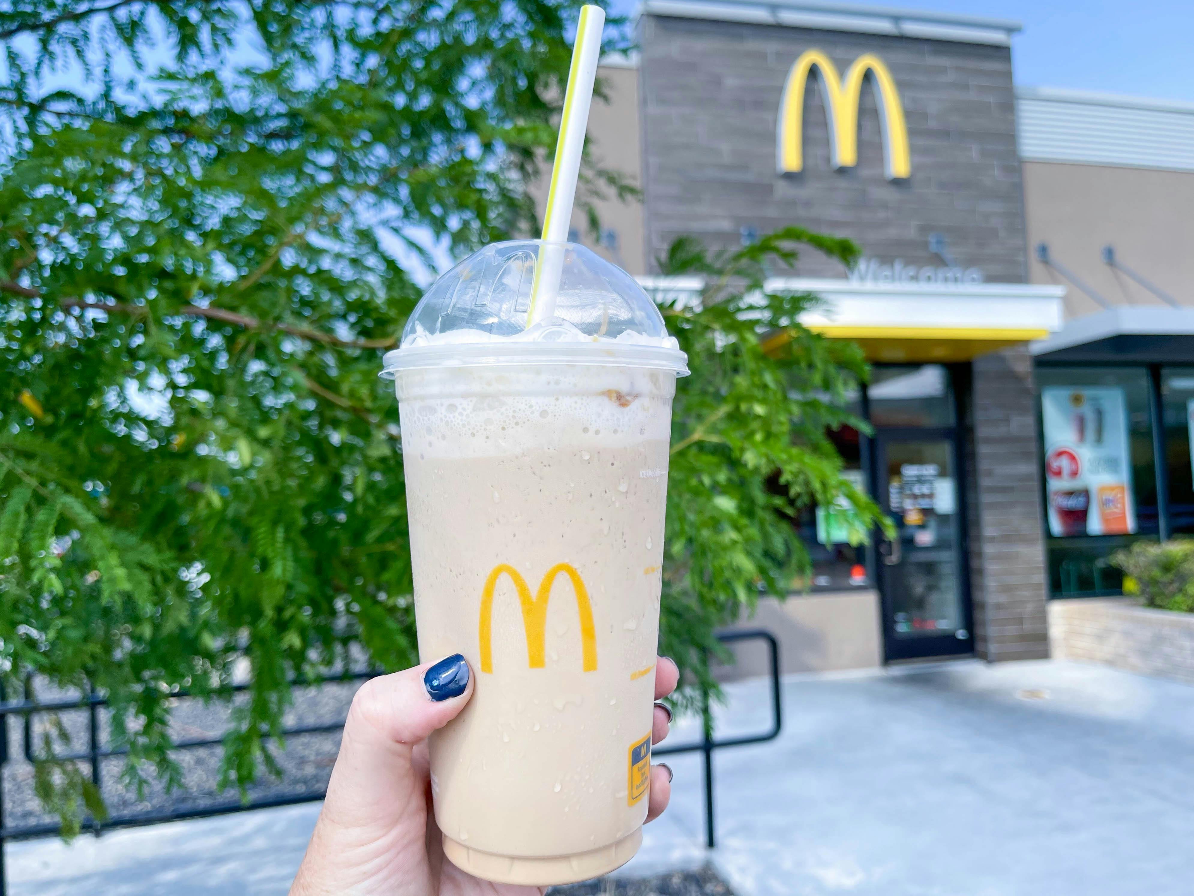 A person's hand holding up a large McDonald's frappe outside of a McDonald's.