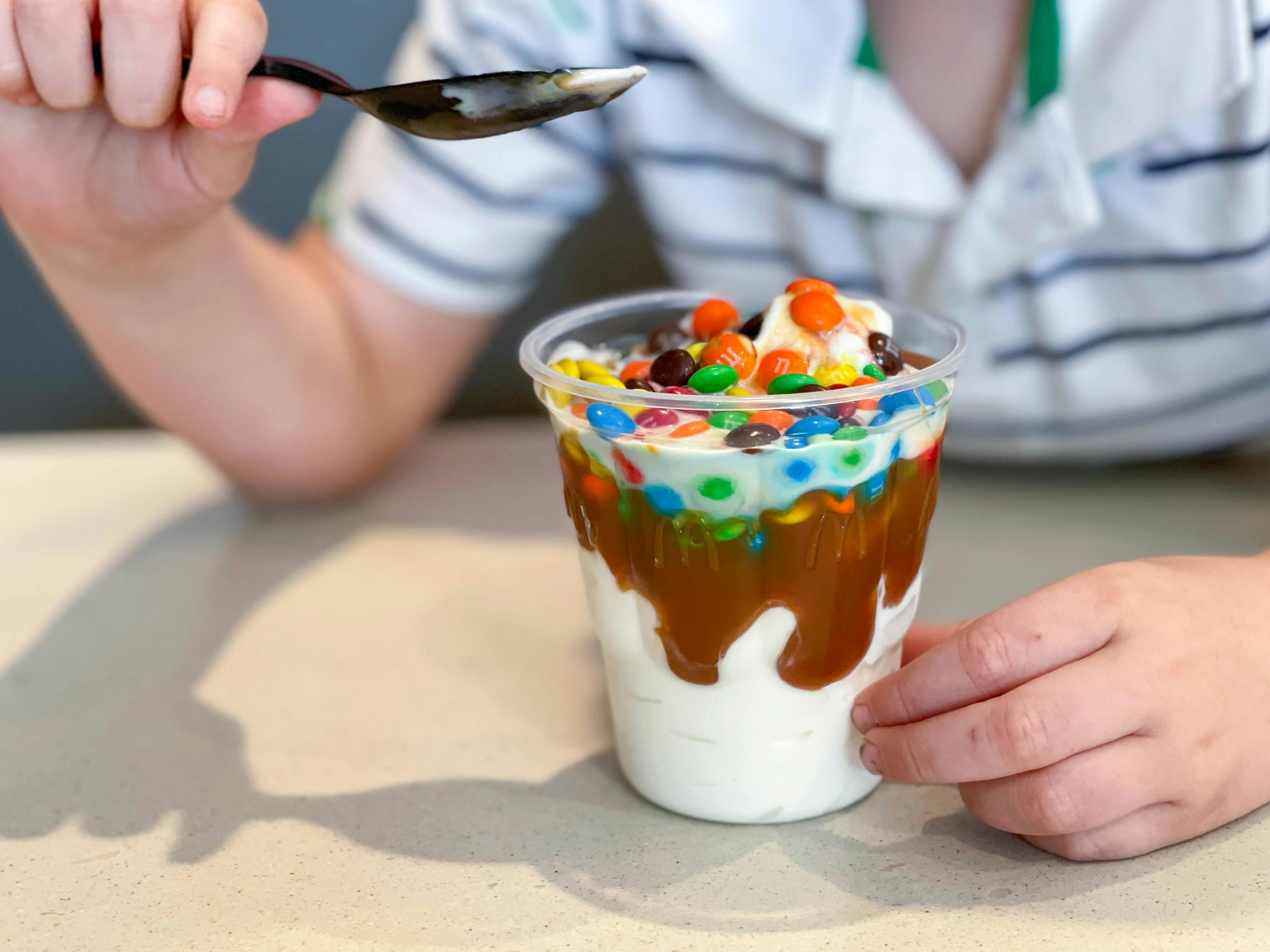 A child using a spoon to eat a sundae with McFlurry toppings at McDonald's.