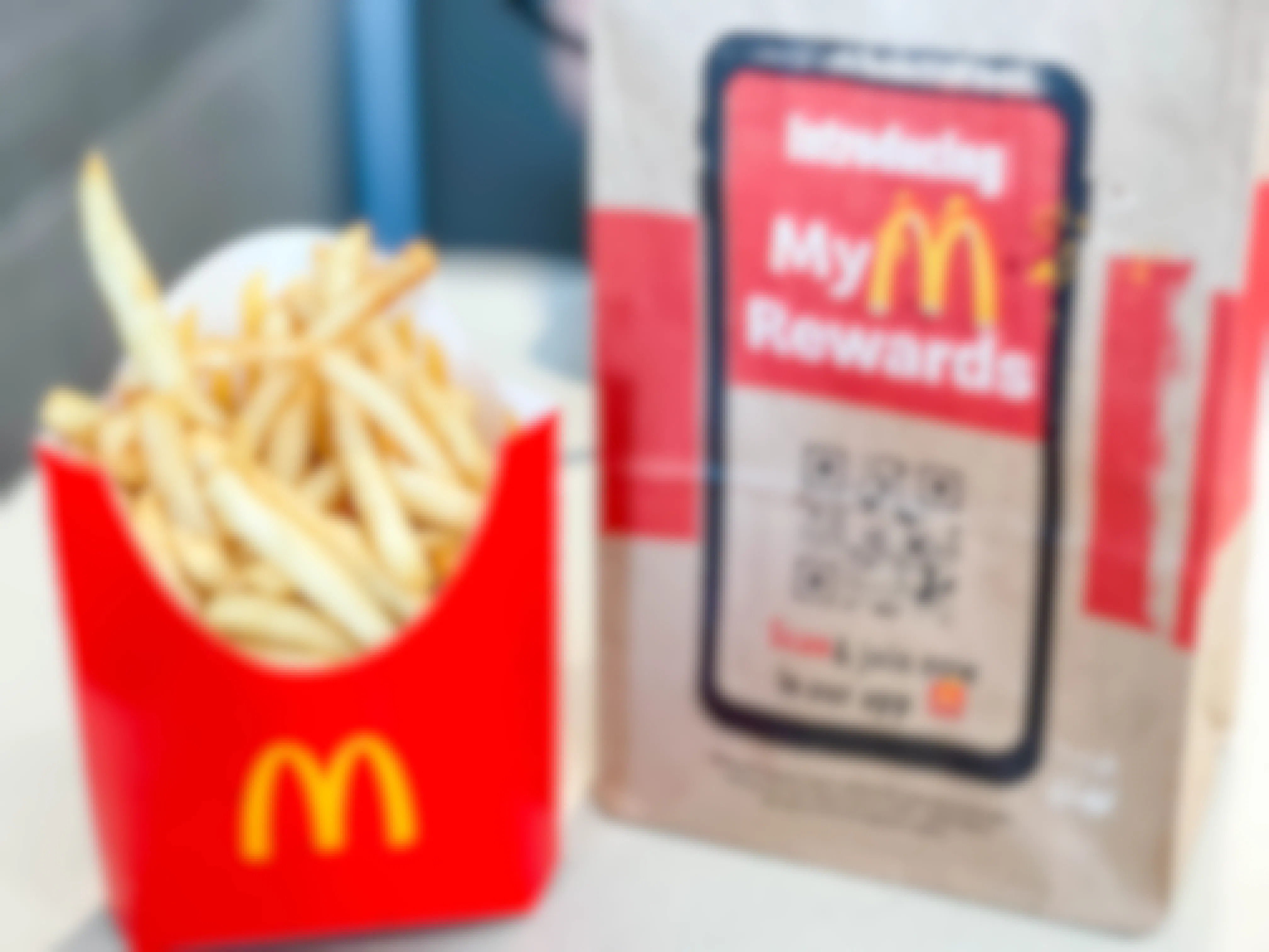 A box of McDonald's fries sitting on a table next to a takeout bag advertising My McDonald's Rewards app with a QR code.