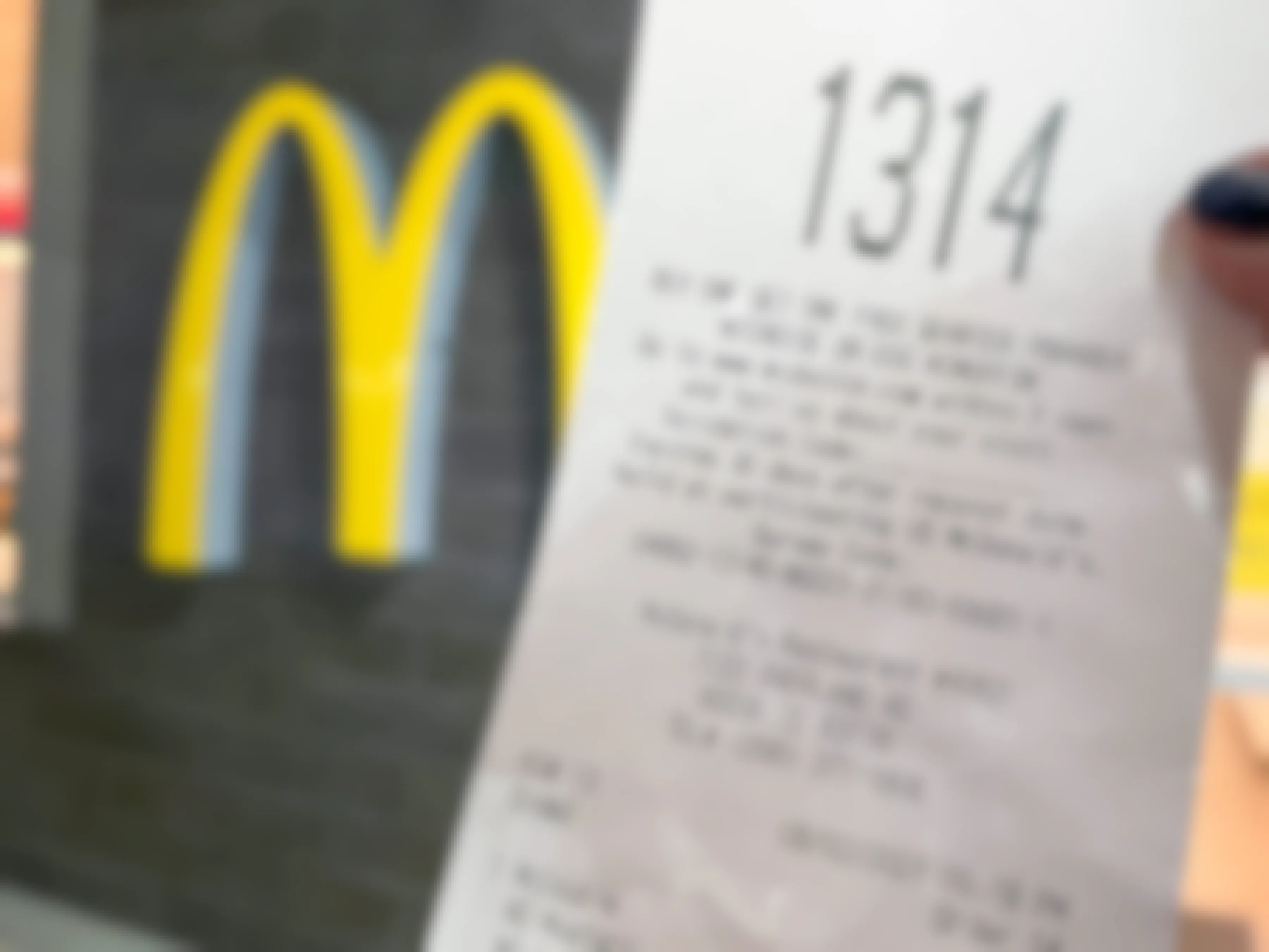 A McDonald's receipt with a survey offer being held up in front of the golden arches logo inside a McDonald's restaurant.