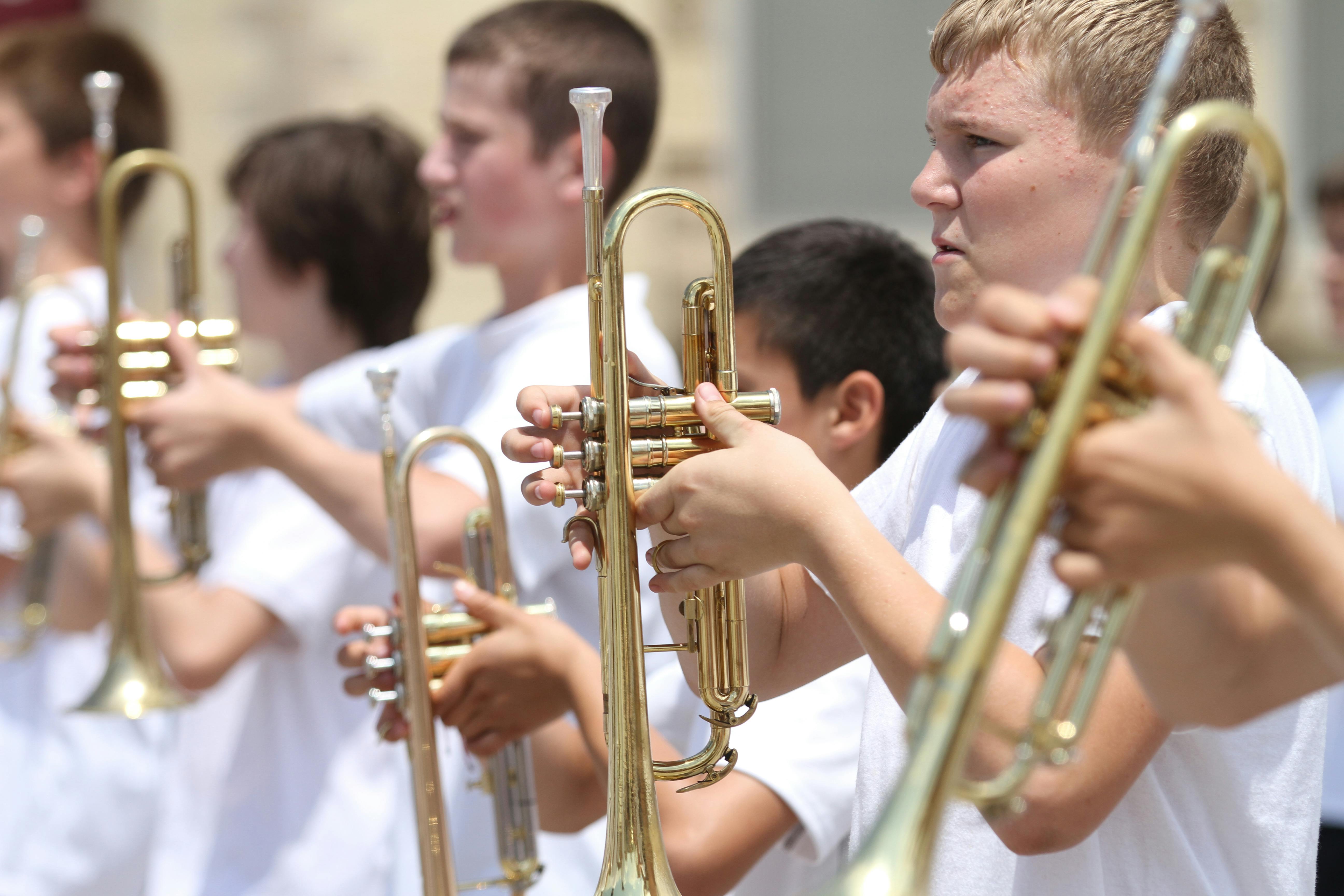 A group of middle school students in white shirts standing in a line and holding trumpets.