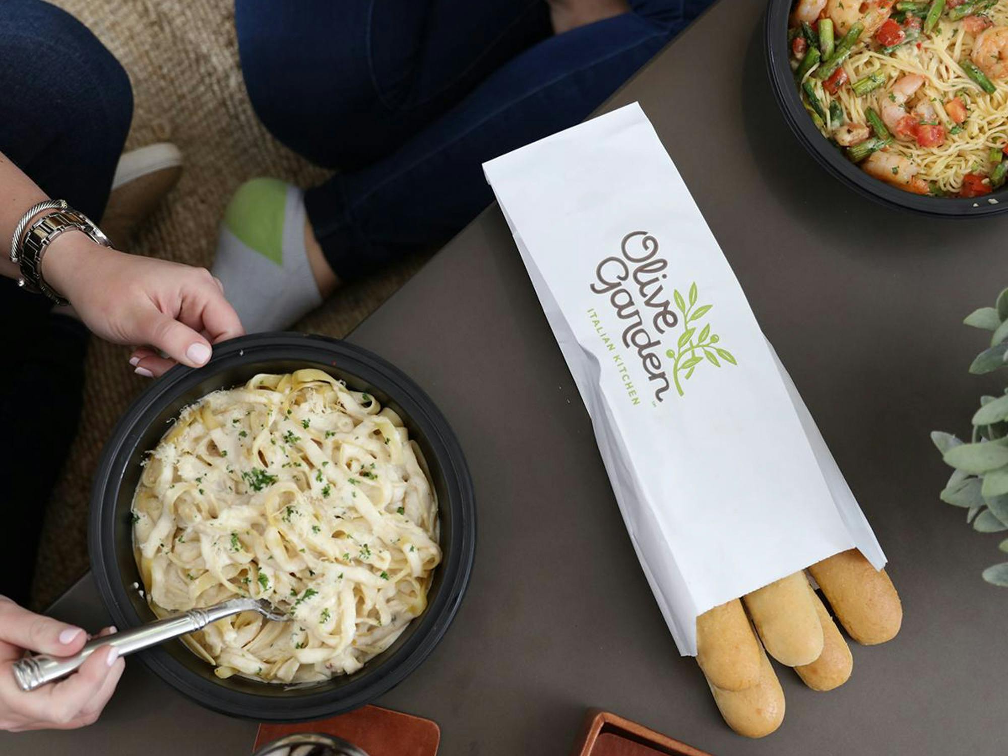 Two people sitting at home enjoying some Take Home Entrees from Olive Garden with breadsticks