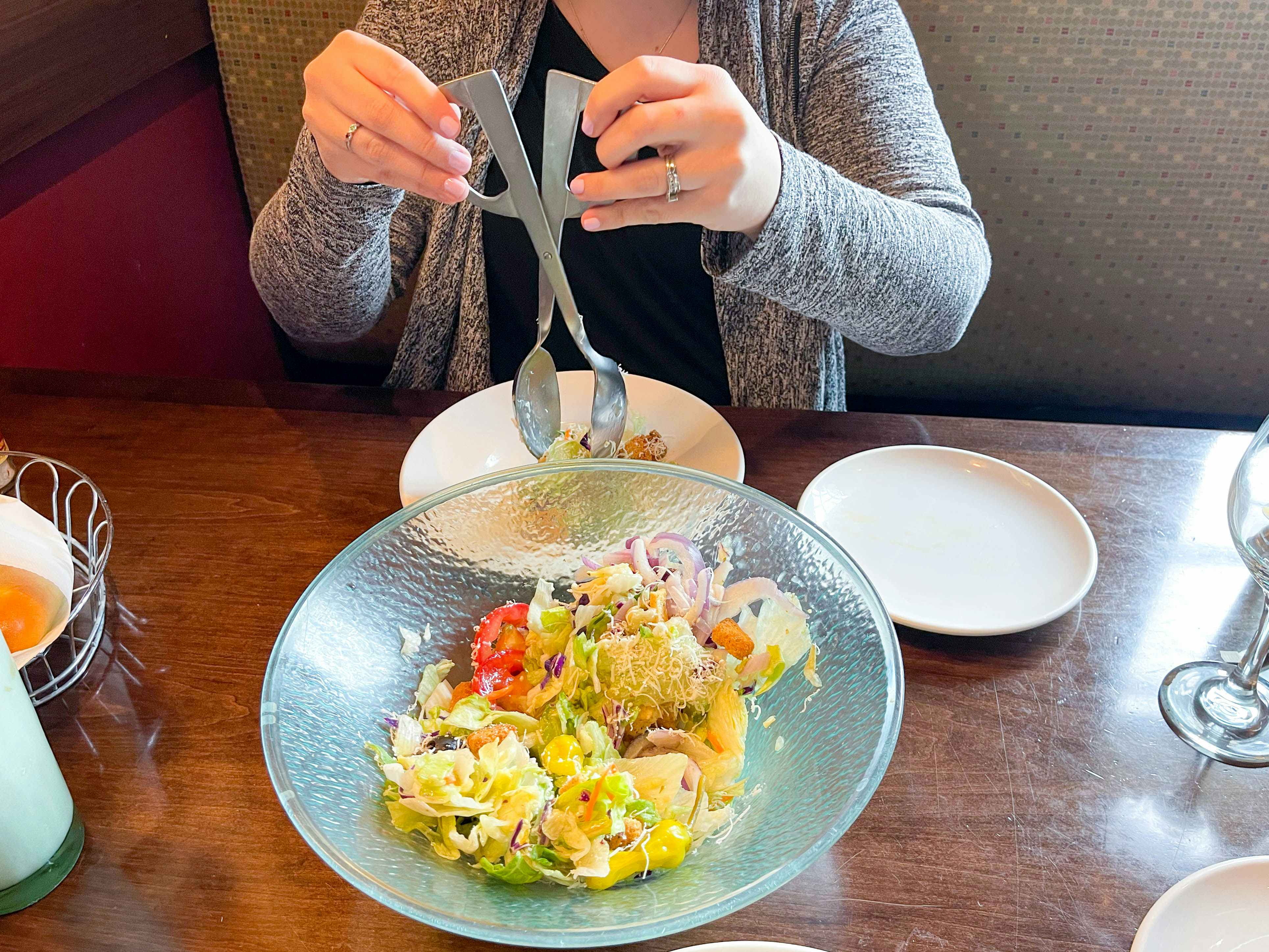 A person using the salad tongs to grab some salad out of the large Olive Garden salad serving bowl.