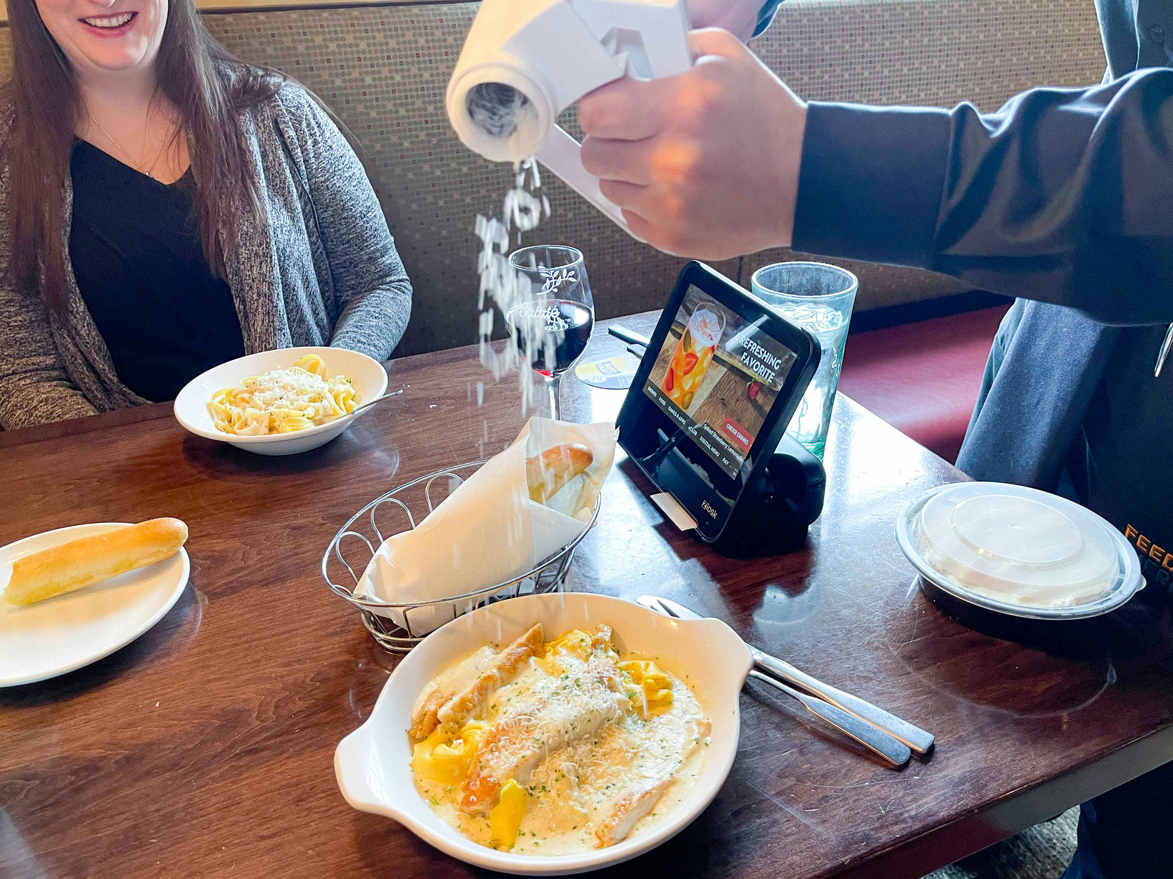 An Olive Garden server grating cheese onto a pasta dish sitting on the table in front of a customer.