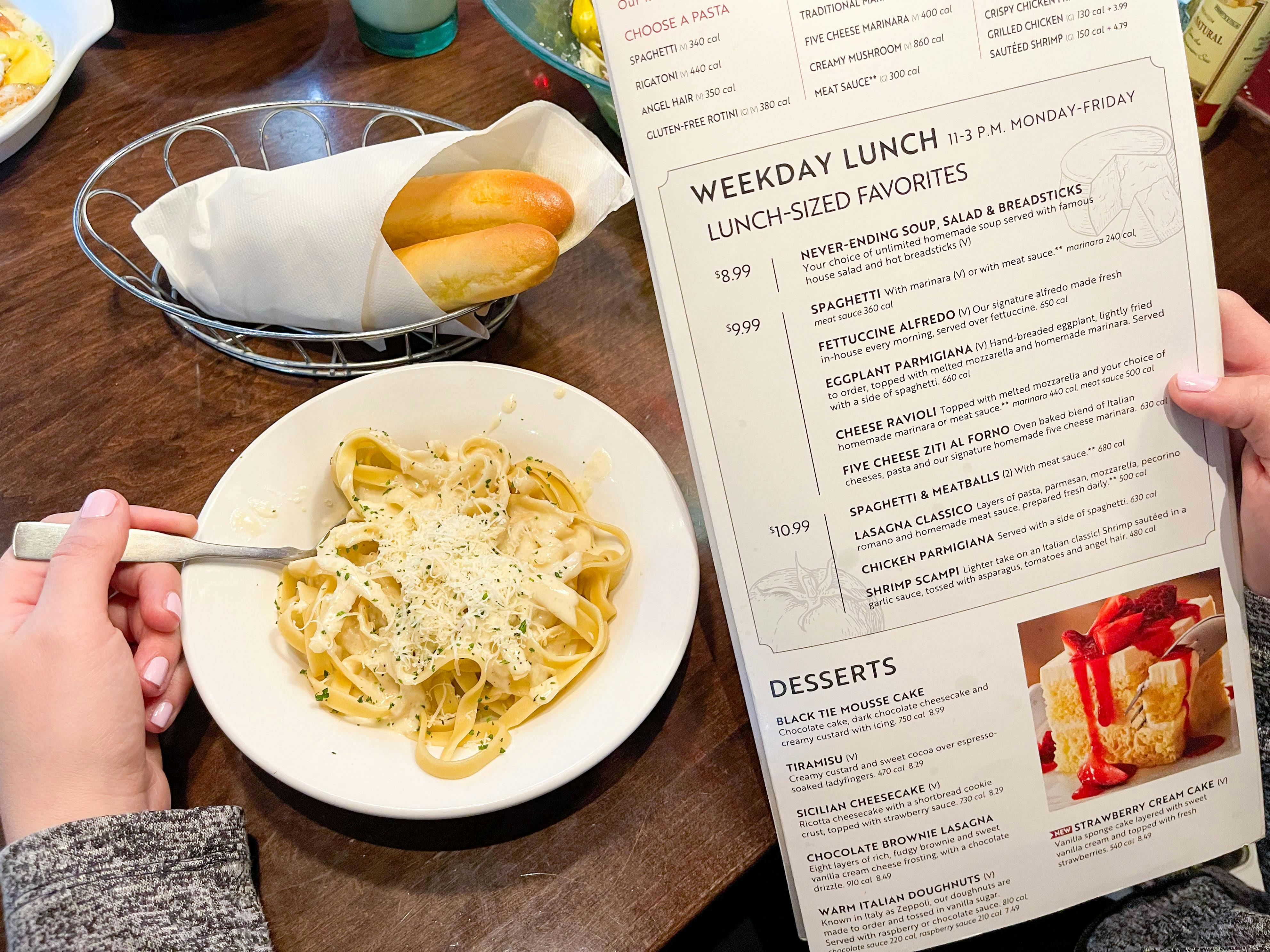 a person scooping food with a fork from a bowl of pasta while looking at a lunch menu 
