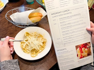 a person scooping food with a fork from a bowl of pasta while looking at a lunch menu