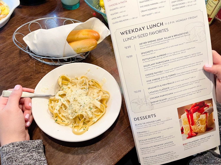 a person scooping food with a fork from a bowl of pasta while looking at a lunch menu 