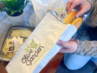 a person pulling out a breadstick from a to go bag from olive garden