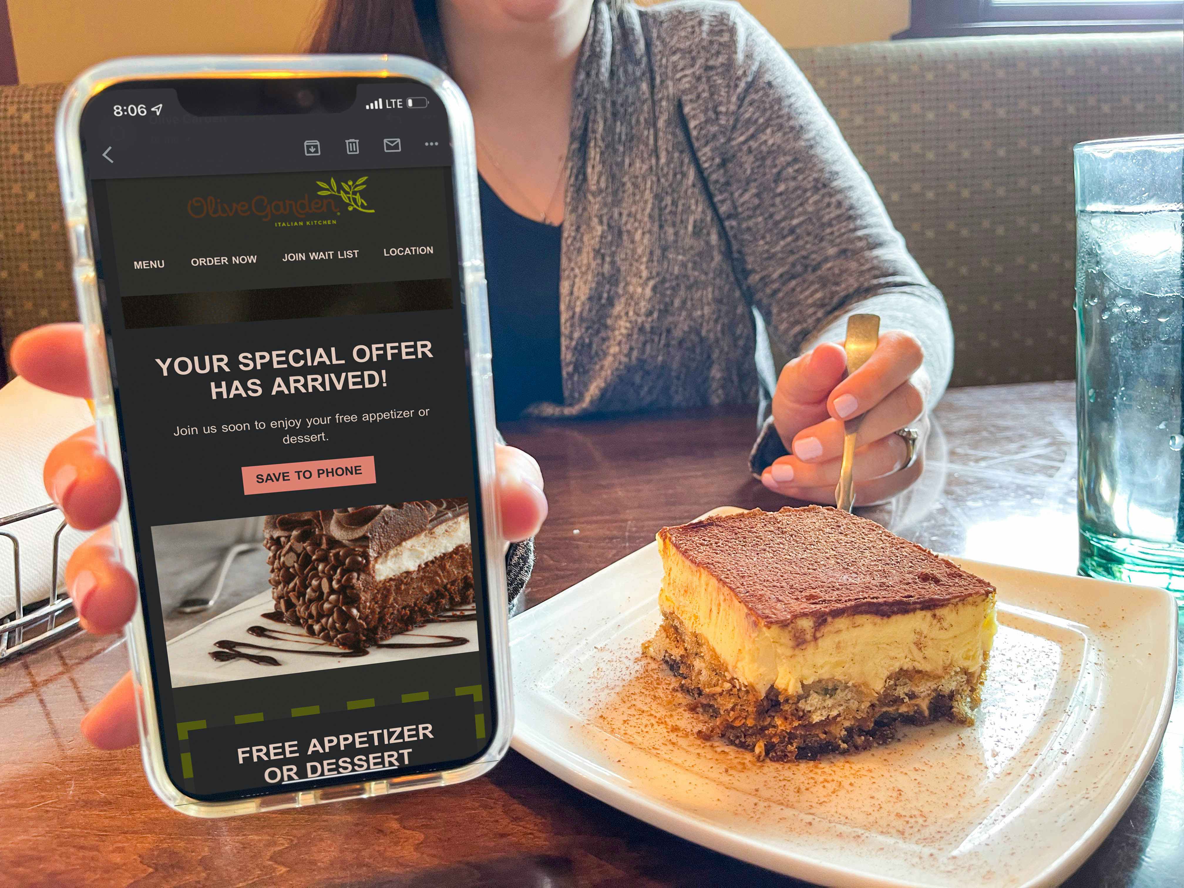 a person holding a coupon on phone app next to an olive garden dessert 