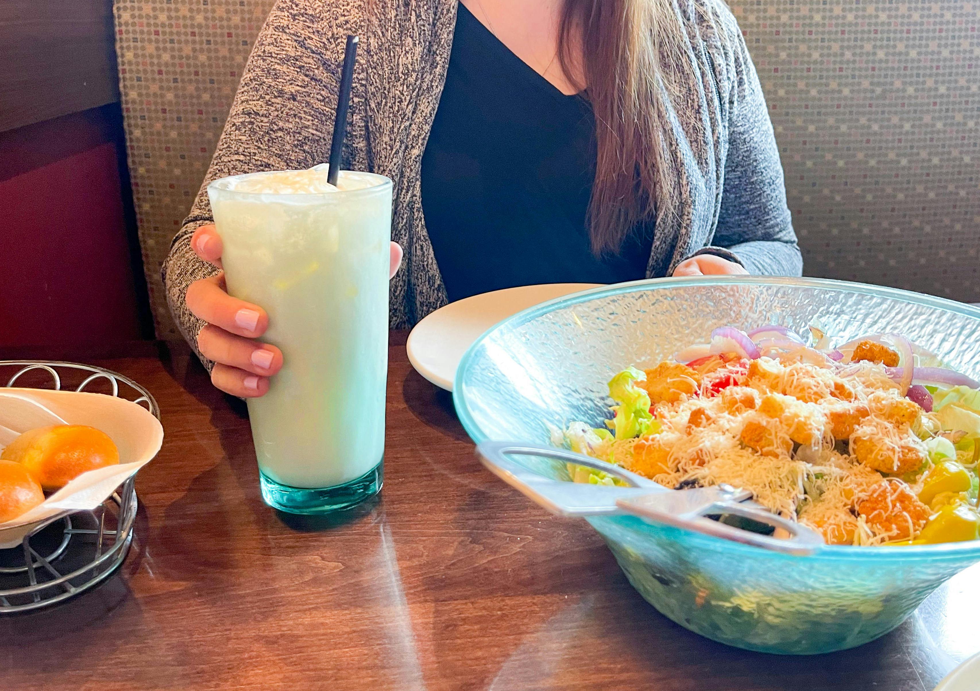 a woman holding a glass of Italian soda near a large bowl of salad 