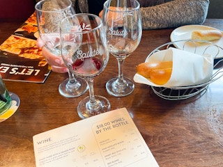 three glasses of wine on a table near to breadsticks and wine menu