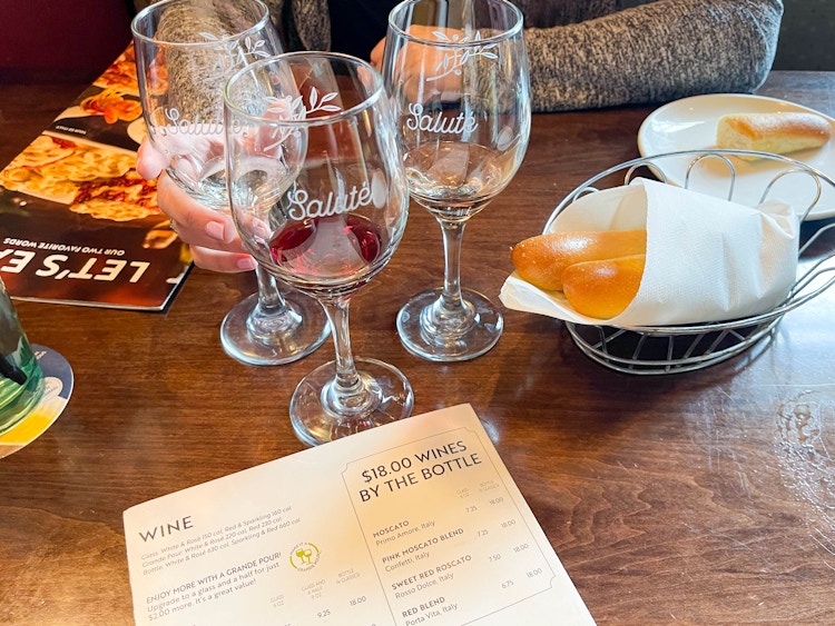 three glasses of wine on a table near to breadsticks and wine menu 