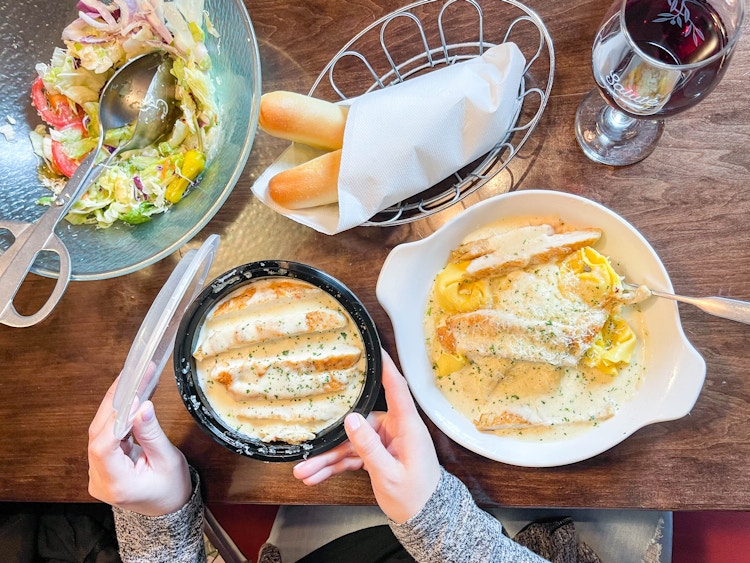 a table full of food with a person putting a lid on a to go container 