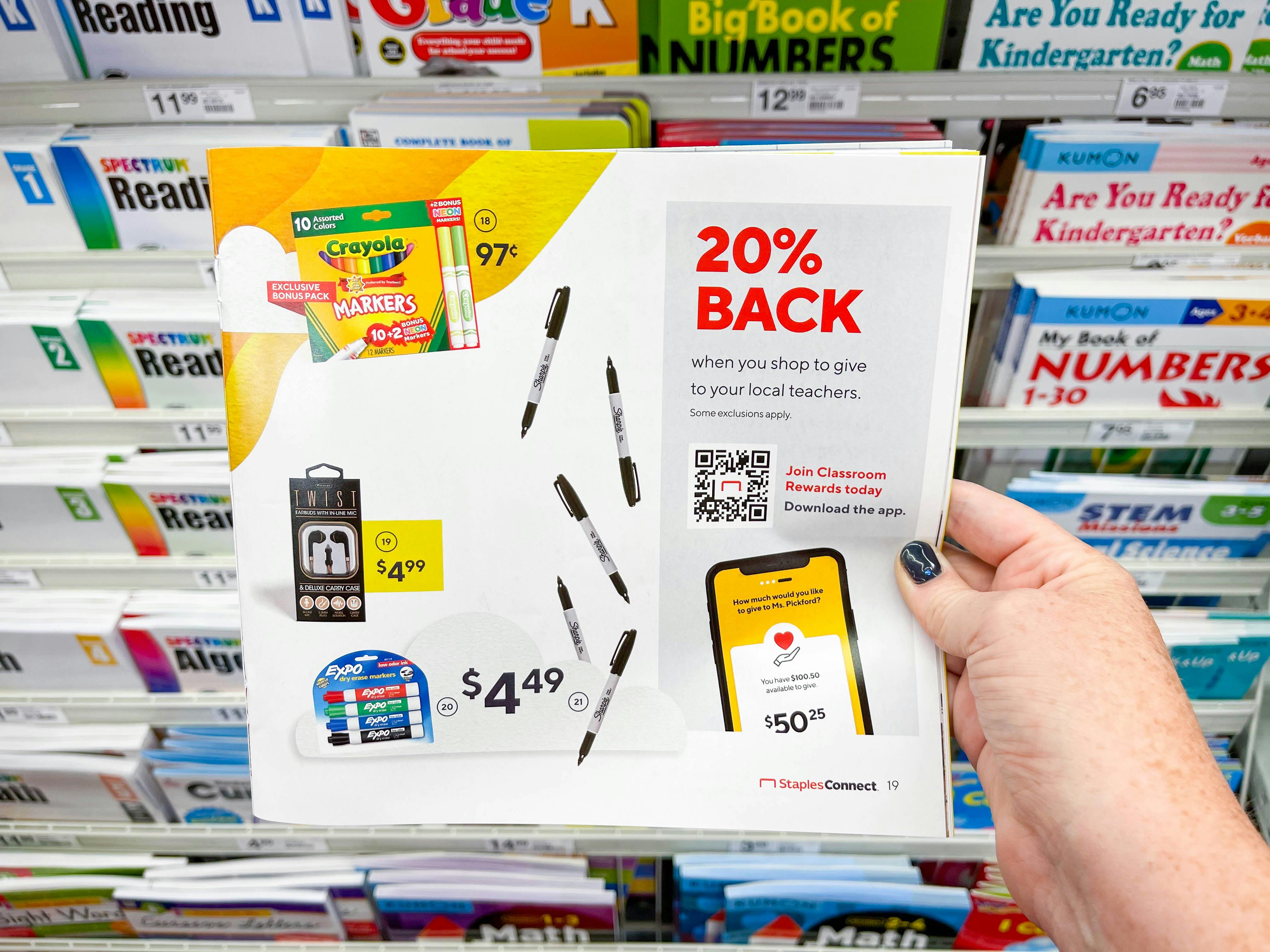 A person's hand holding up a paper advertisement for Classroom Rewards at Staples.