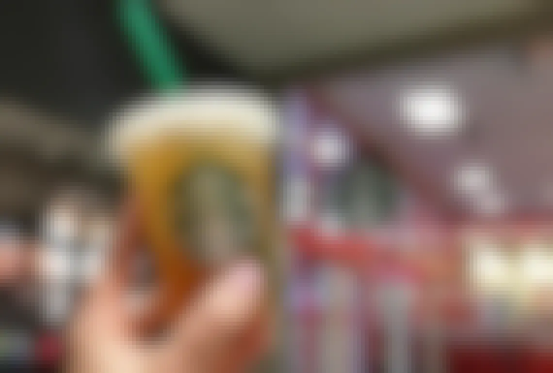 A person's hand holding up a Starbucks iced tea in front of a Starbucks sign.