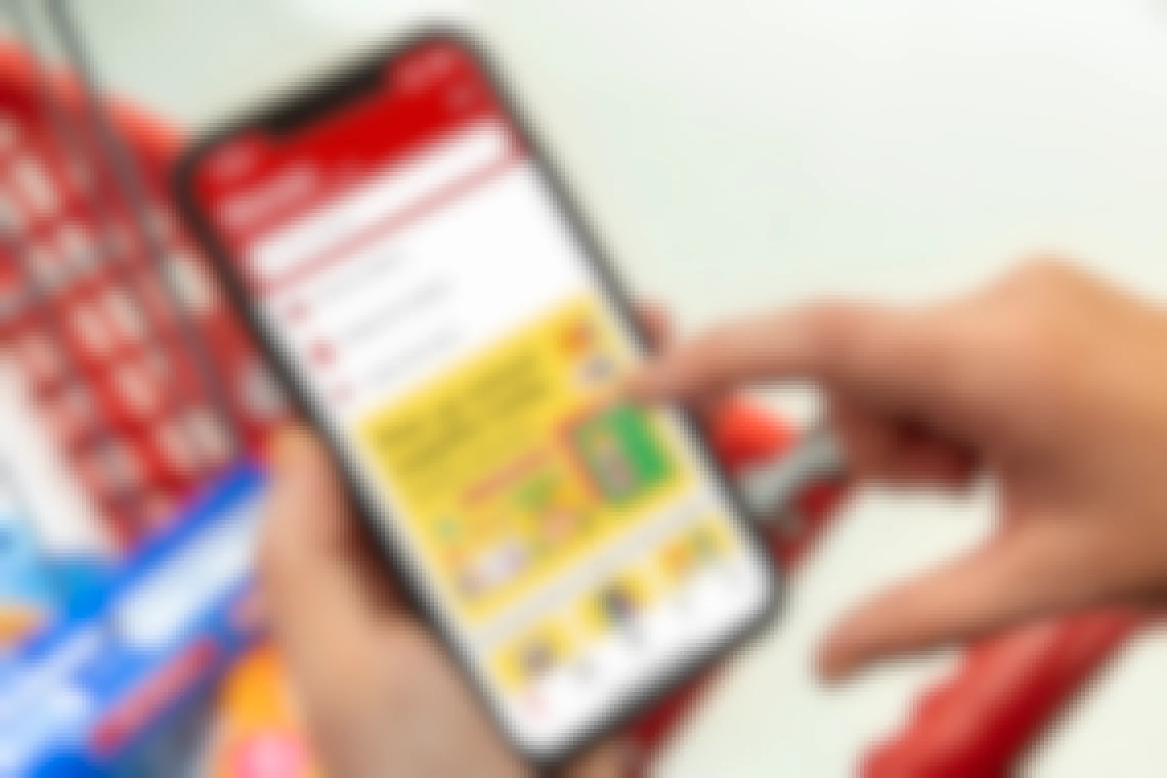 A person's hands holding a phone above a Target shopping cart with the Target app's back to school page open on the screen.
