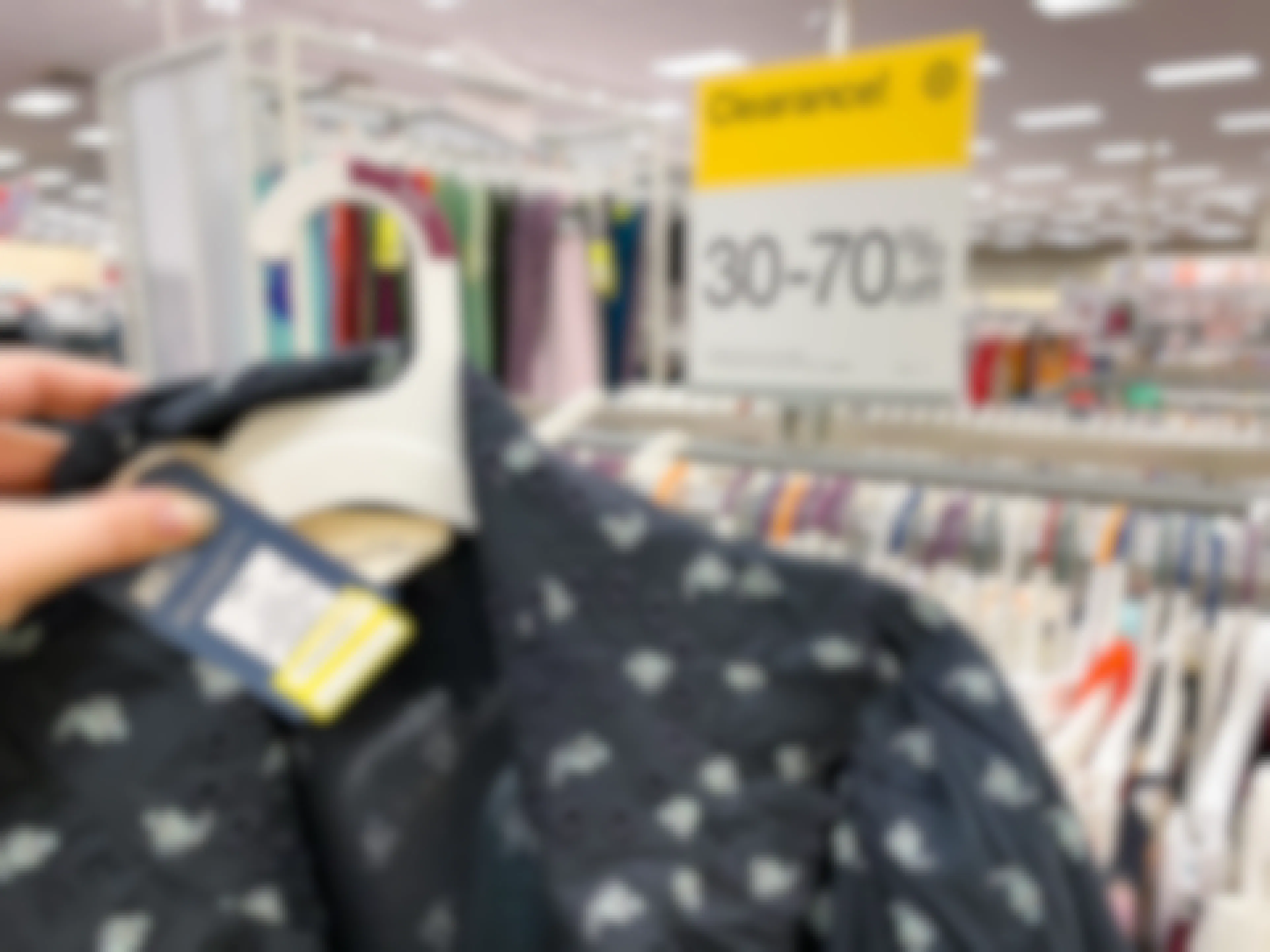 A clearance shirt being held up in front of a clearance sign on a clothing rack in Target