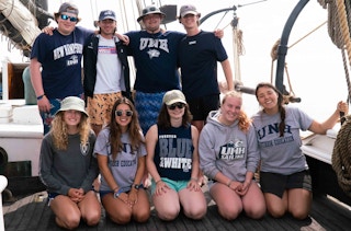 A group of students from University of New Hampshire posing for a photo on the deck of a boat.
