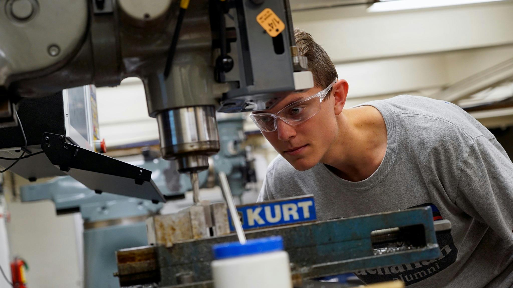 A student at Webb Institute wearing safety glasses and using a drill press.