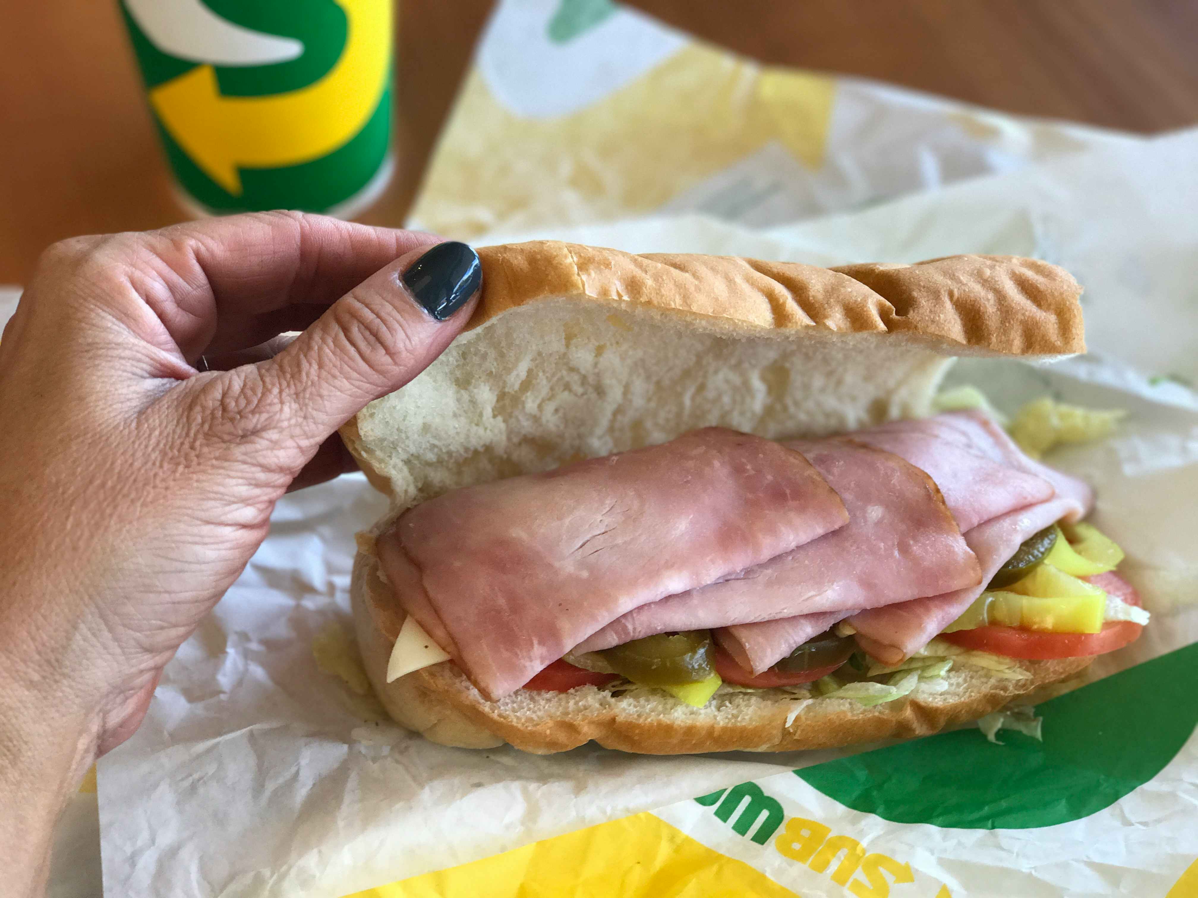 woman's hand opens a subway sub to reveal ingredients