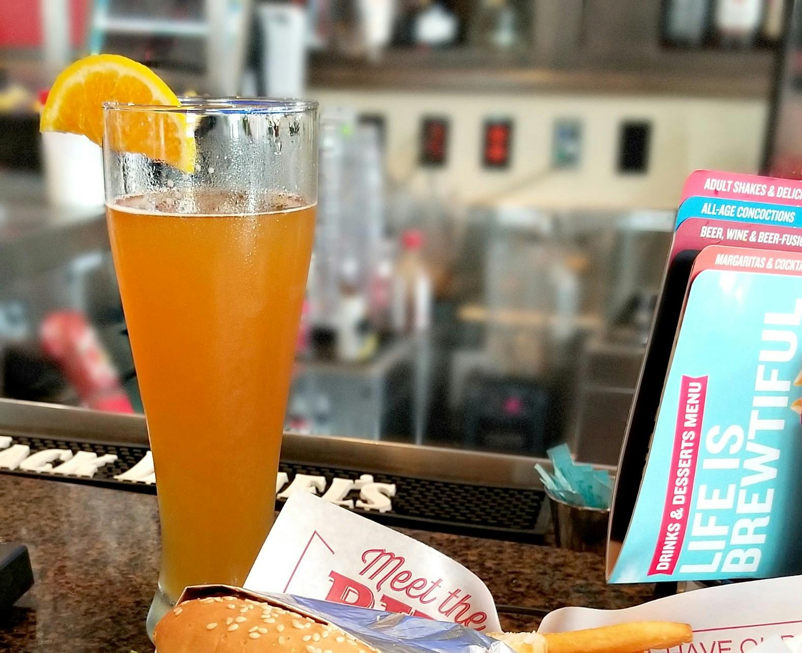 A glass of beer with an orange slice on the rim sitting on the bar counter at Red Robin.