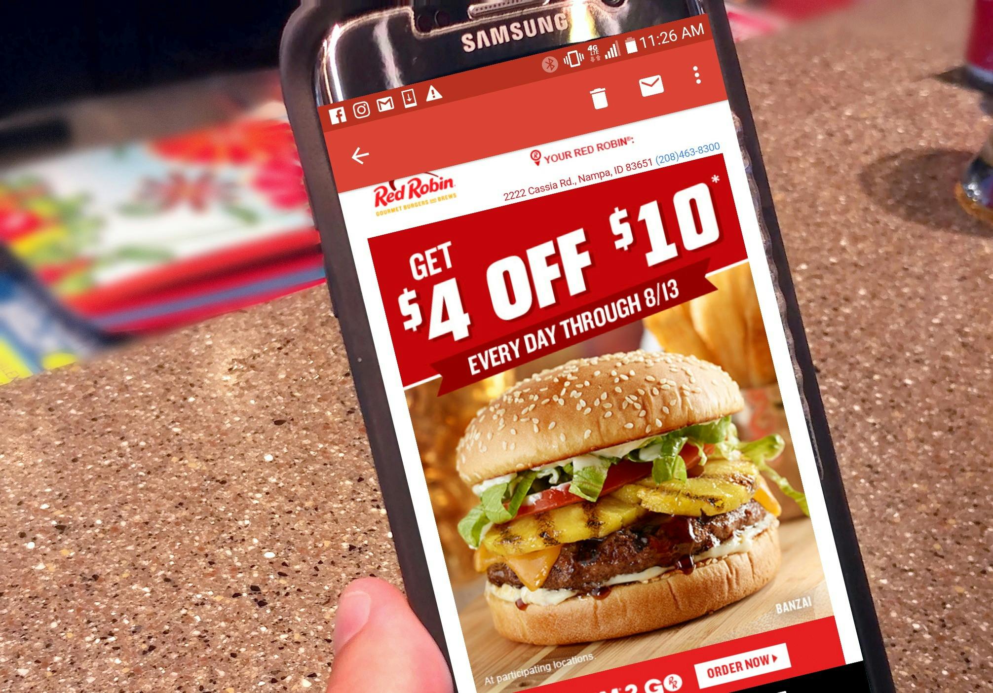 A person's hand holding up a cell phone with the Red Robin mobile app open to the Royalty Rewards offers.