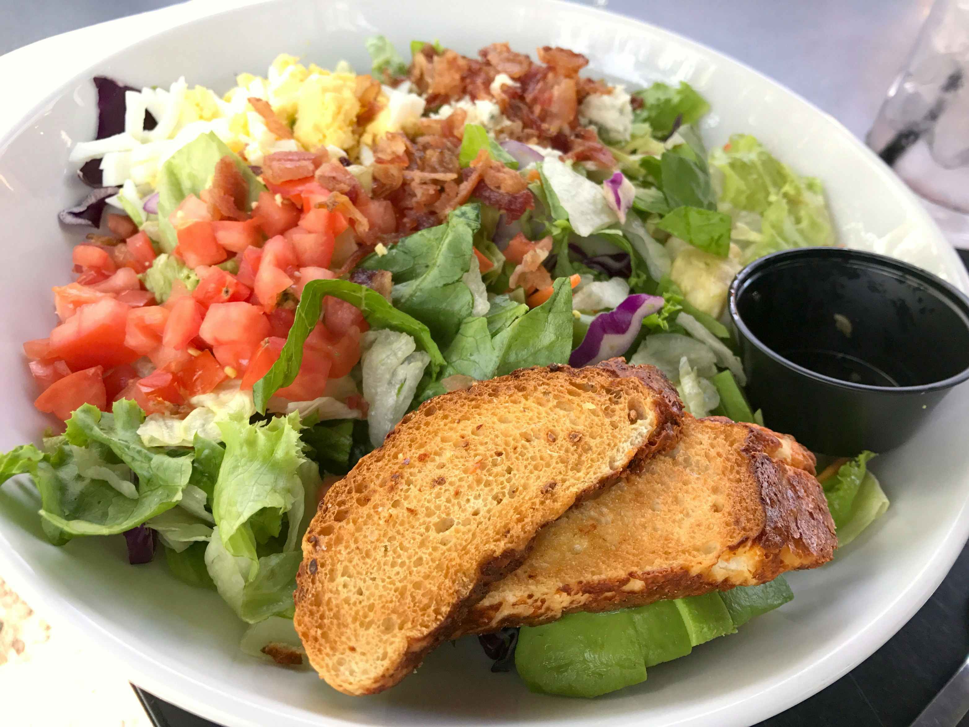 A close-up of a Red Robin salad with a dressing cup and two small pieces of bread.