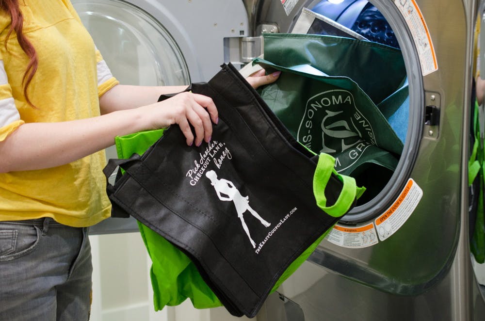 A woman throwing reusable grocery bags into a front load washing machine.