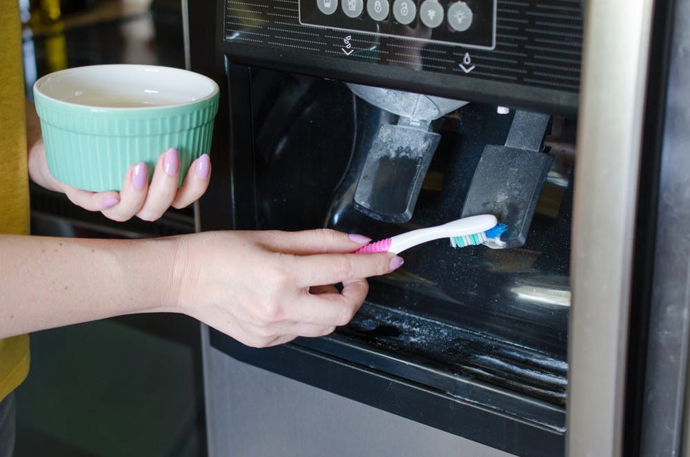 someone scrubbing refrigerator dispenser pedals with toothbrush