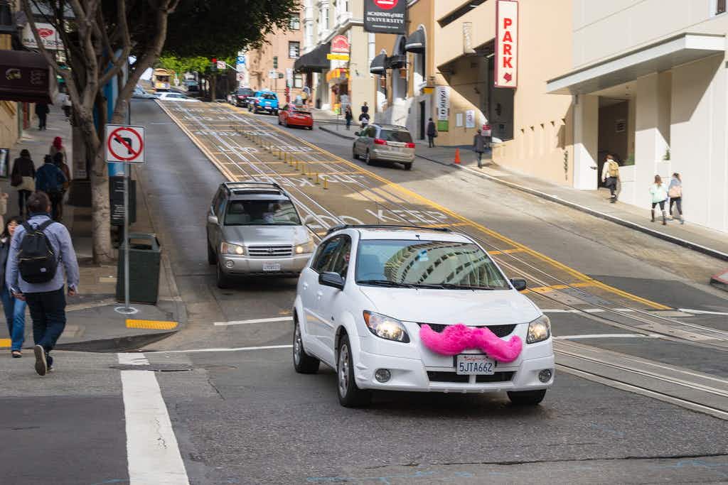 a car with a pink mustache driving down the road 