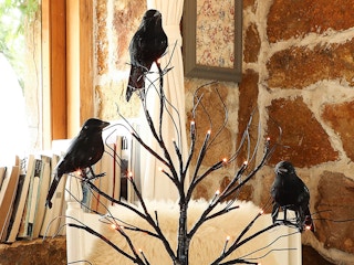 Faux crows perched on a tree decoration with LED lights in the branches.