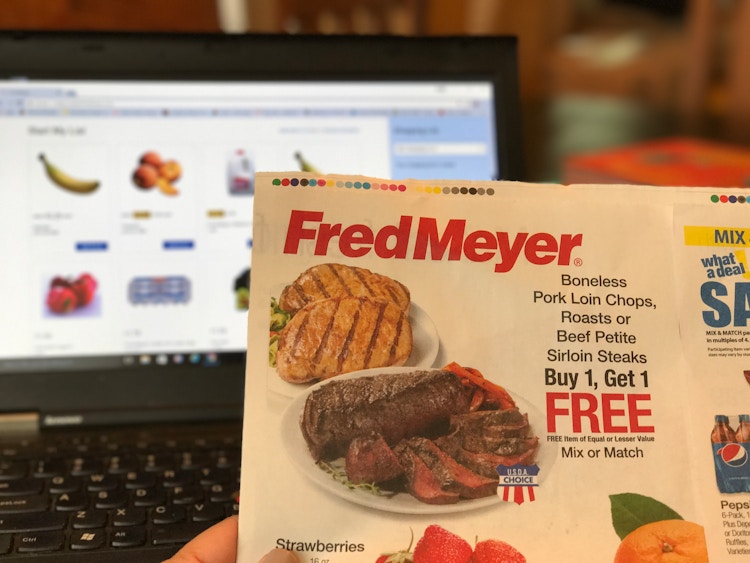 hand holds up fred meyer ad to fred meyer online grocery site