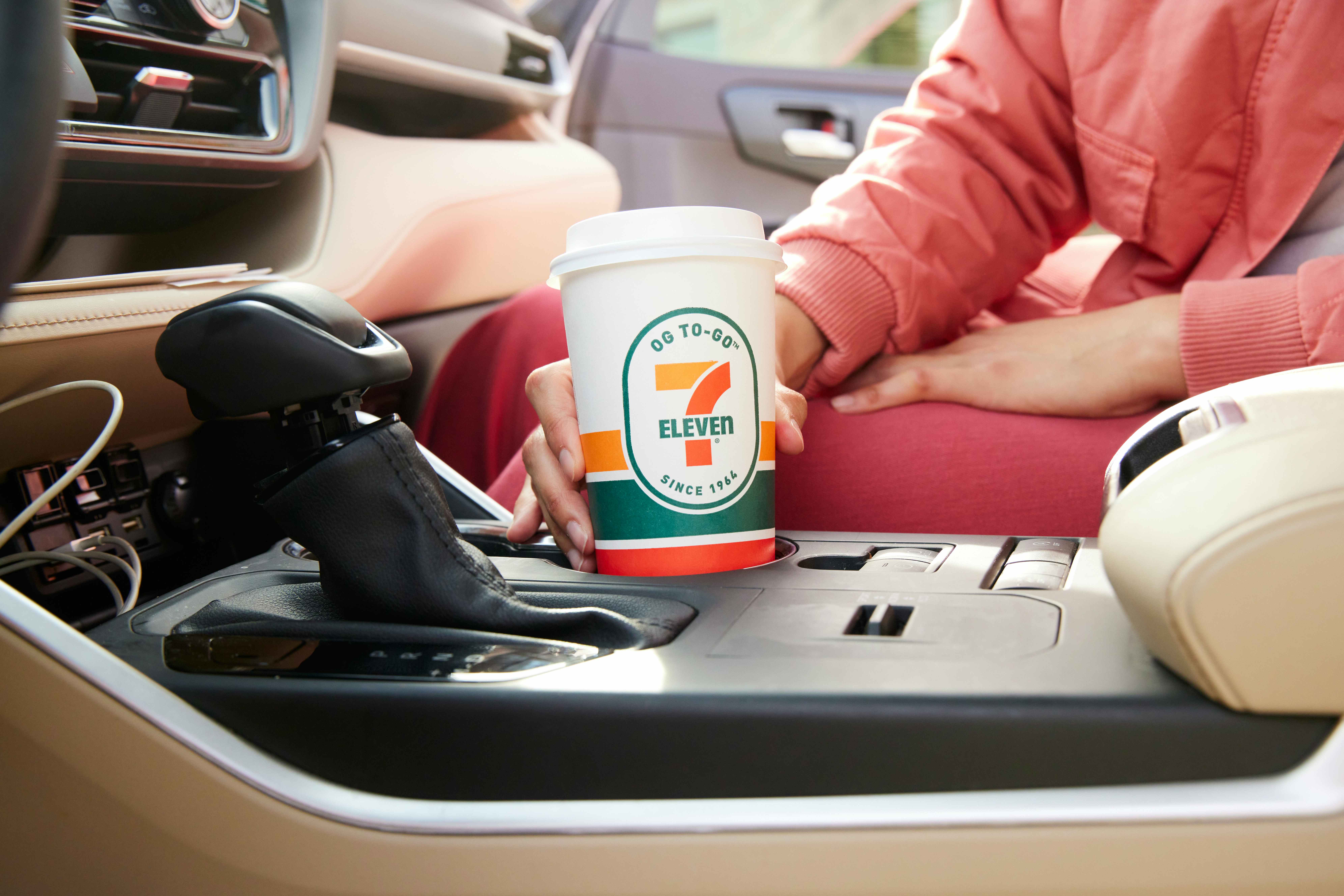 A person holding a 7-Eleven coffee cup inside a vehicle.