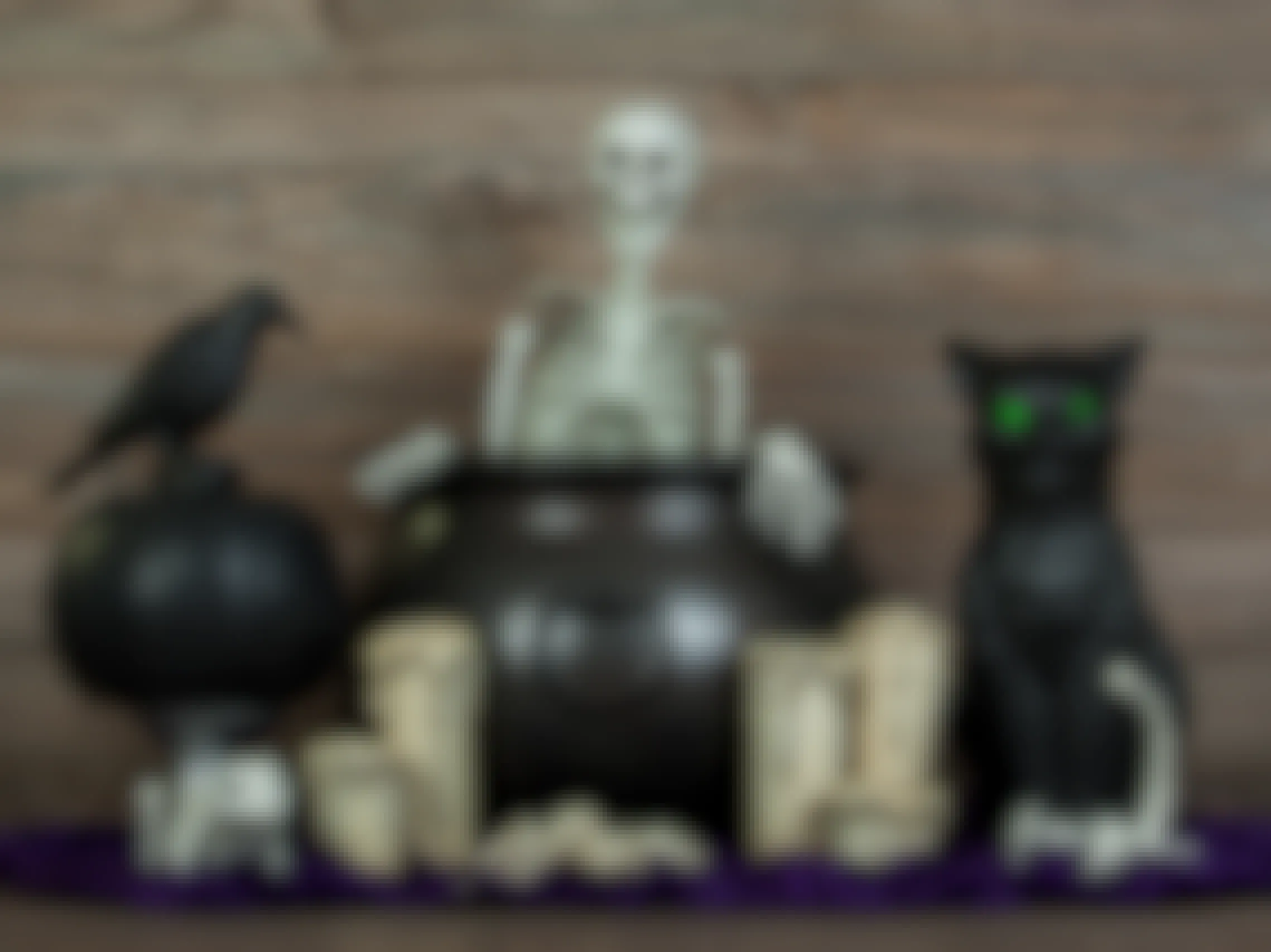 Halloween decorations grouped together on a table including a cauldron, a skeleton, a crow, a black cat, some candles, and more.