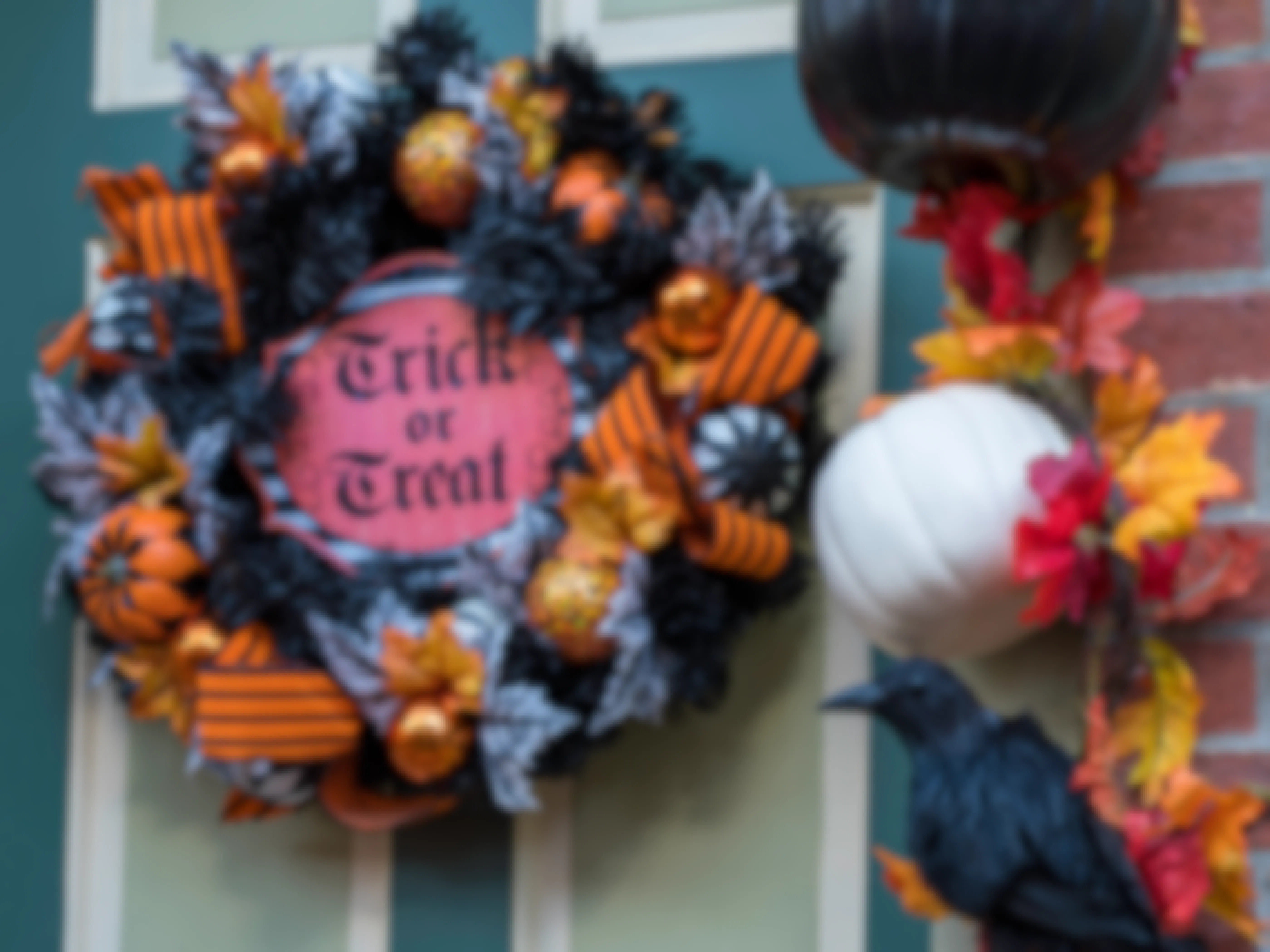 A Trick-or-Treat wreath hung on a front door near other Halloween decorations.