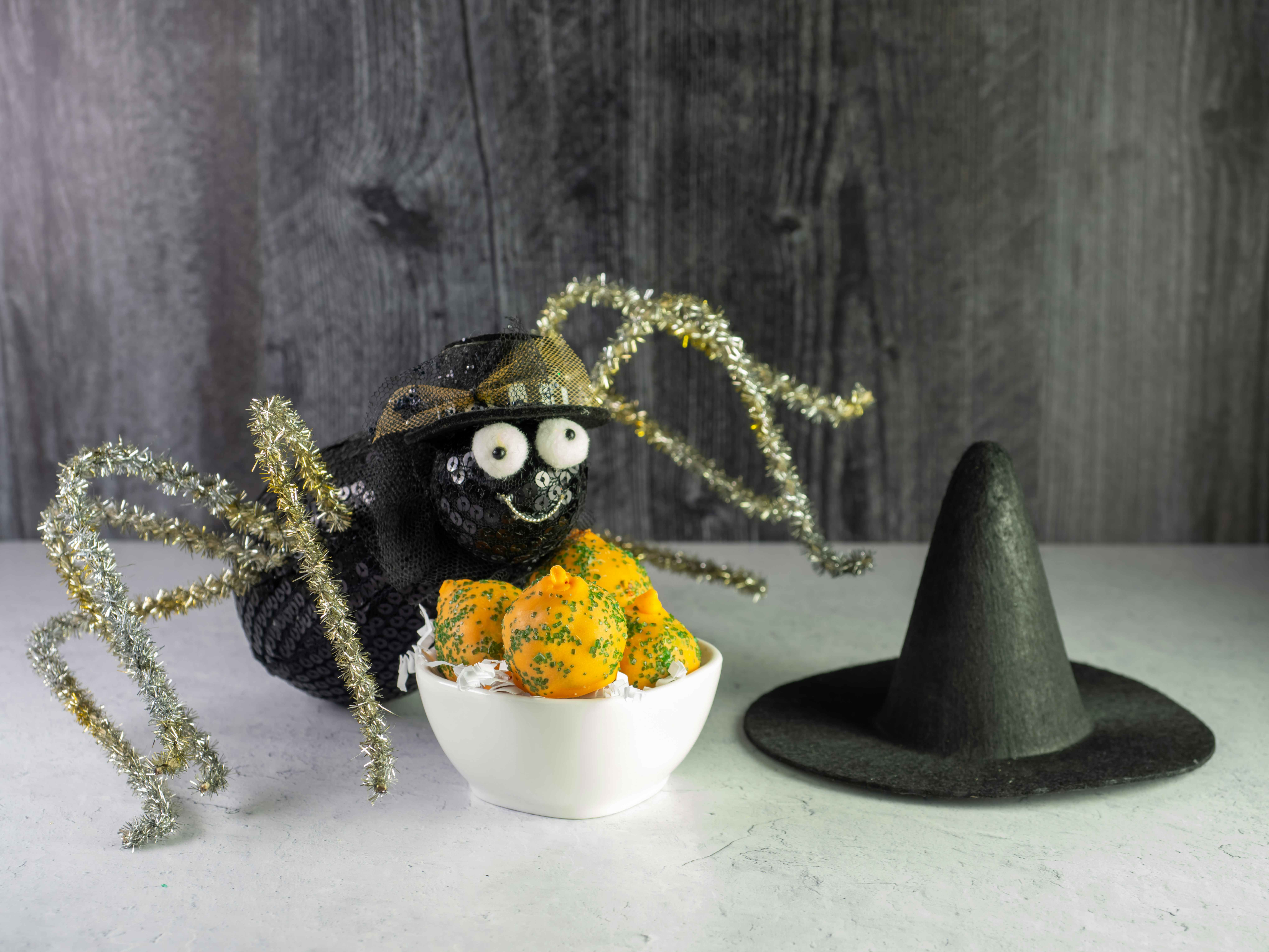 A crafted spider sitting on a table next to some treats and a little witch hat.