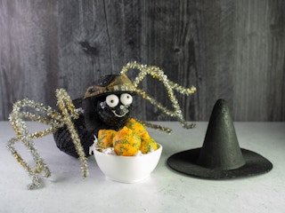 A crafted spider sitting on a table next to some treats and a little witch hat.