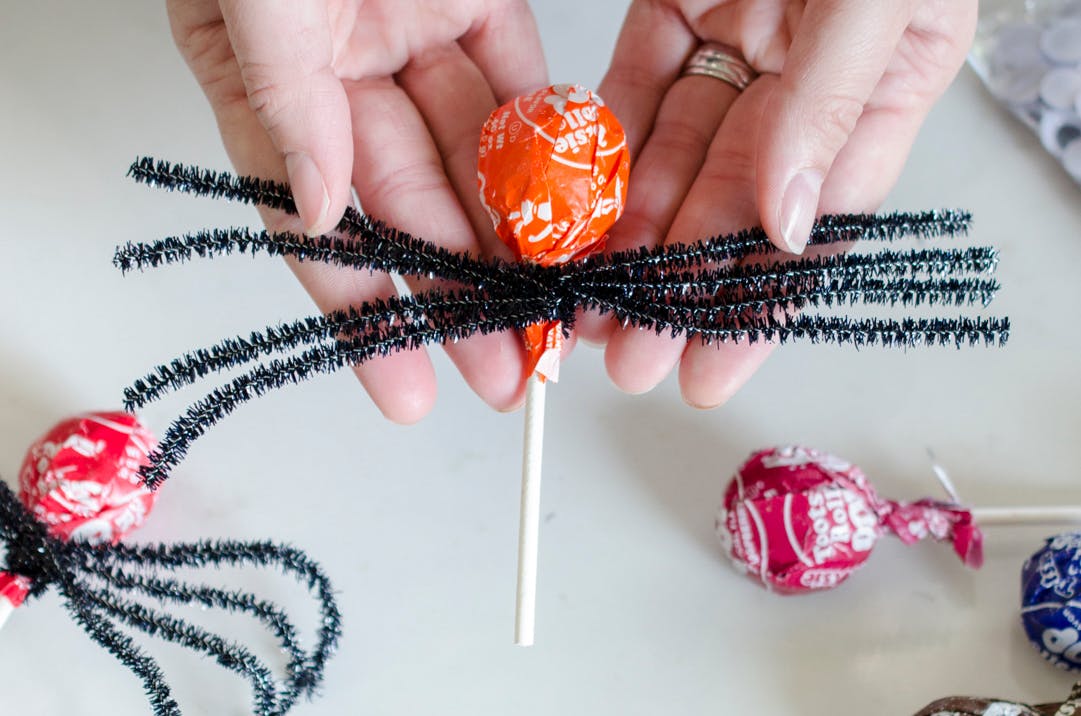 Pipe cleaners being twisted around a lollipop candy. 