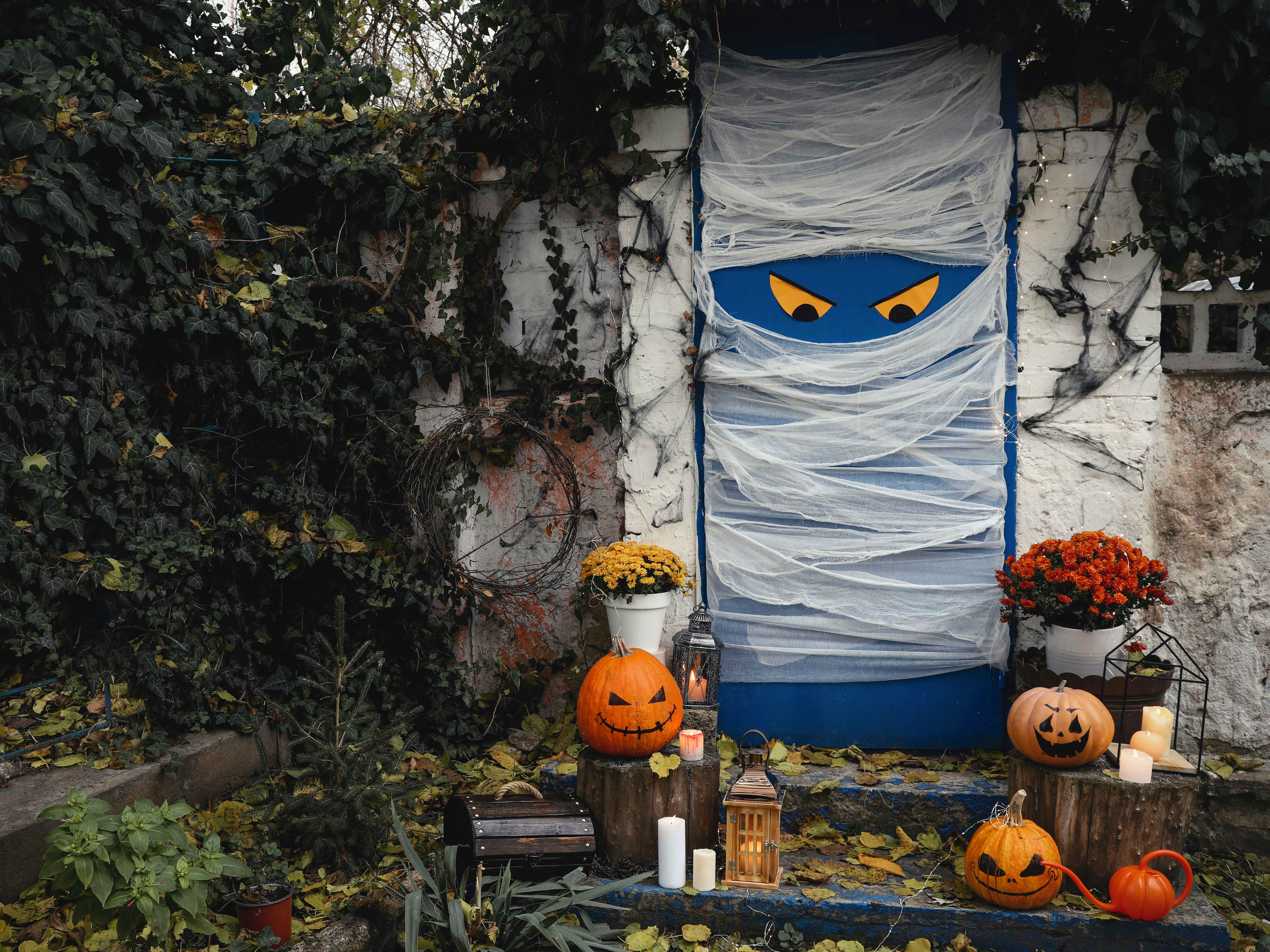 A front door decorated to look like a mummy with Halloween decorations on the steps leading up the porch.